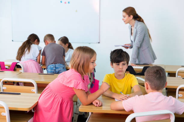 Interested preteen pupils discussing learning material in groups stock photo