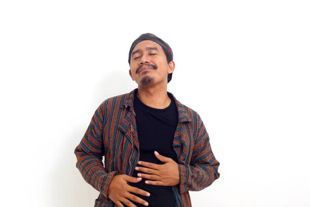 Asian man standing while touching his stomach, fells full, satisfied. Isolated on white background