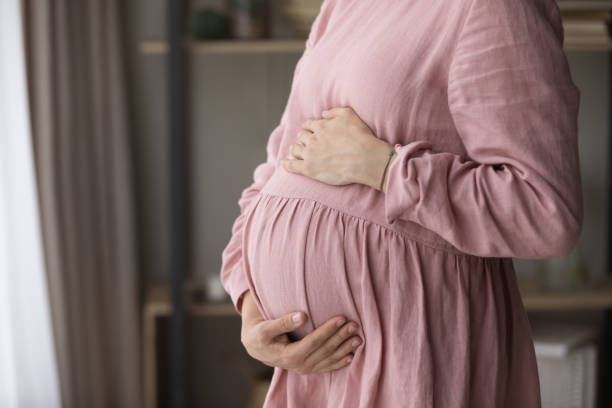 istock Unknown pregnant woman standing indoor touch her big belly 1407372000