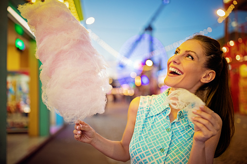 Young woman is eating cotton candy at a funfair