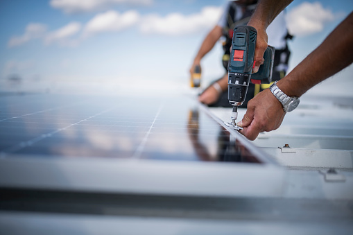 Close up of hands of a worker installing solar panel system using drill.