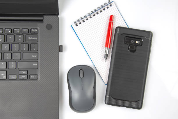 istock Computer wireless mouse, pen and notepad next to a laptop on a white table close-up. Items for office work 1407385518