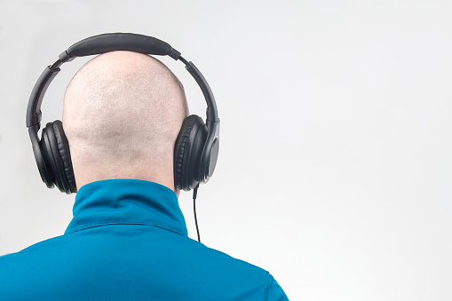 back of the head of a man with headphones in relaxation listening to music on a light background.