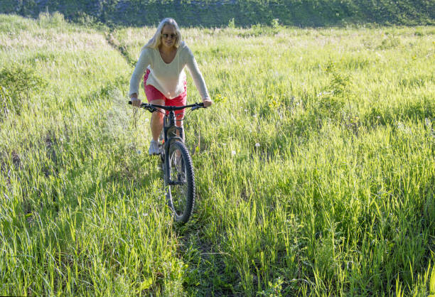 istock Mature woman e-bikes through lush grasses, 1407389848