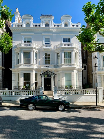 Holland Park street view. A beautiful Victorian or Edwardian house with parked retro car near Holland Park. Stunning exterior of Grand white stucco villa. Shades on the road. Central London, England, UK