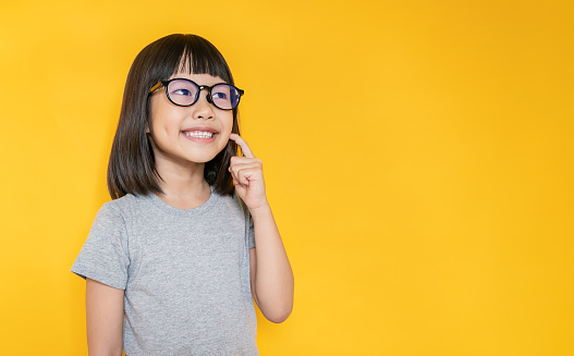 Portrait of young fun smart happy little cute asian girl isolated on yellow with copy space studio shot. Education for elementary kindergarten, little girl wear glasses thinking back to school concept