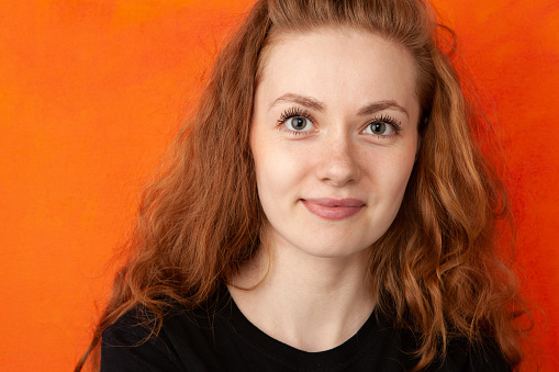 Close-up studio portrait of an attractive 24 year old red-haired woman in a black t-shirt on an orange background