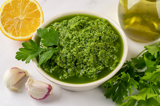 Chimichurri dipping sauce in a bowl. Fresh green sauce from parsley, garlic cloves, olive oil and lemon juice. Homemade salsa verde with fresh herb and spices. Cooking healthy condiment. Close-up.