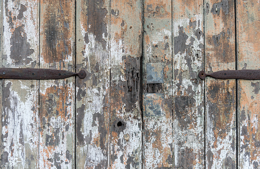 Old wooden doors with old layers of paint, and with a rusty metal hinge.