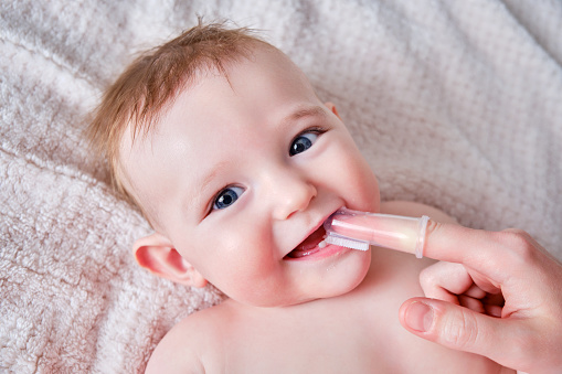 La madre se cepilla los dientes con un cepillo de dedos de un bebé feliz. Mamá haciendo higiene bucal a un niño sonriente, de seis a siete meses de edad photo