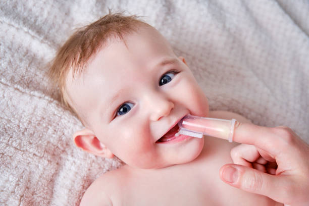 la madre se cepilla los dientes con un cepillo de dedos de un bebé feliz. mamá haciendo higiene bucal a un niño sonriente, de seis a siete meses de edad - 6 11 meses fotografías e imágenes de stock