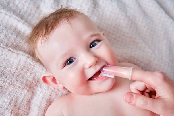 Mother hands brushing teeth with a finger brush of a happy infant baby. Mom doing oral hygiene to a smiling toddler kid, six to seven months old Mother hands brushing teeth with a finger brush of a happy infant baby. Mom doing oral hygiene to a smiling toddler kid, six to seven months old half dozen babies stock pictures, royalty-free photos & images