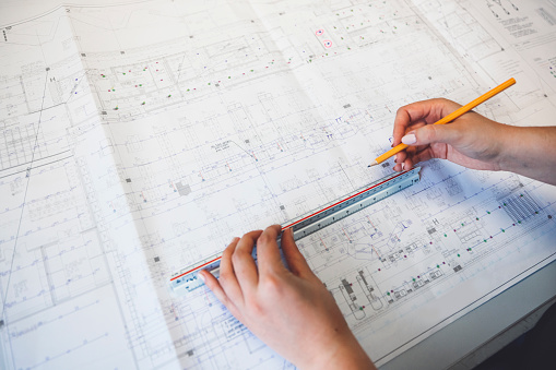 Unrecognizable woman hands drawing on a blueprint using a ruler.