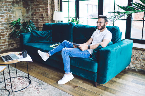 istock Cheerful young man with tablet resting on sofa 1407415415