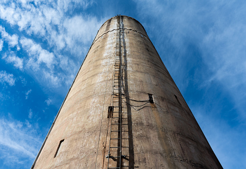 Tall, old water tower with ladder bisecting and leading to the top. Back drop of bright, blue sky and cloud wisps.