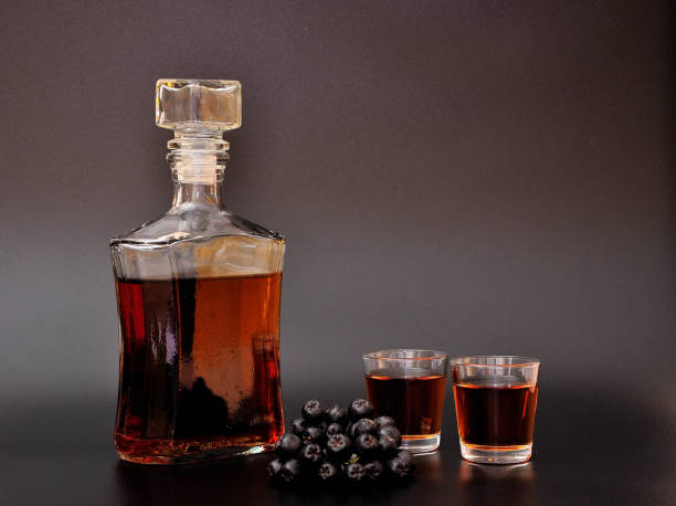 아로니아 리큐어, 강한 수제 알코올 및 검은 배경에 잘 익은 정원 열매의 가지. - juice carafe glass decanter 뉴스 사진 이미지