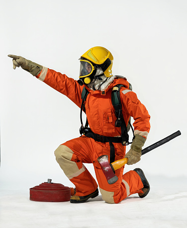 One Firemenan weraing heat protection suit and helmet breathing with oxygentank on white background hold axe and hose stand still action portrait action on fire fighting