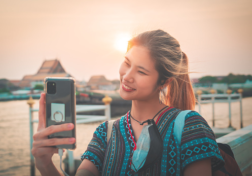 Female tourist is taking selfie photo using mobile phone in Bangkok Chao Phraya river view street walk, Thailand.