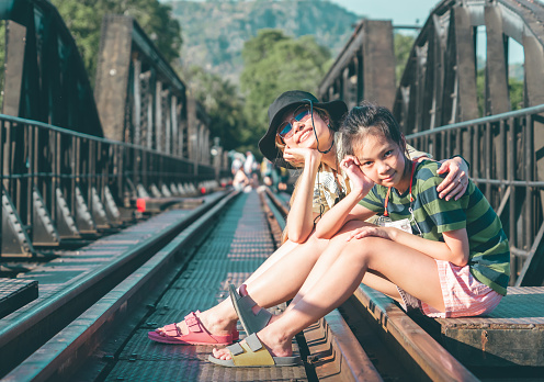 Mother and child is sitting the historical bridge of World War 2 in River Kwai. Kanchanaburi Thailand.