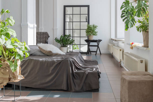 istock Modern bright living space with large windows, bed, mirror, work desk and decorative flowers. 1407433701