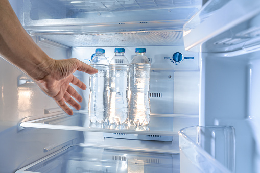 A shaky thirsty male's hand reaching out to grab a cold water bottle from a refrigerator, with motion blur effect added to the hand