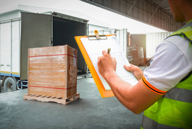 istock Worker Holds a Clipboard Controlling the Loading of Cargo into Shipping containers. Packaging Boxes Goods. Loading Dock. Distribution Warehouse Cargo Logistics. Freight Truck Transport. 1407441990