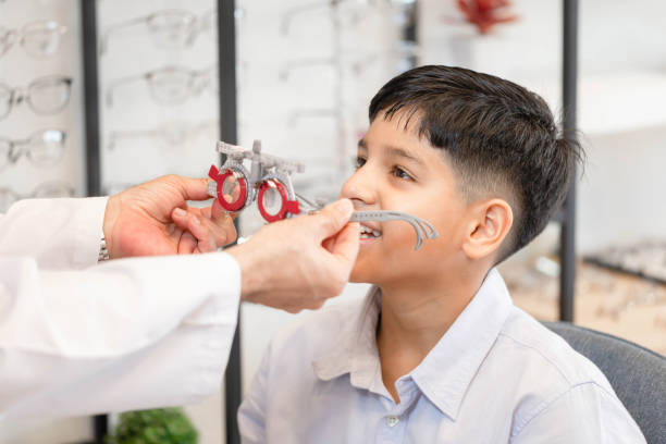 istock Cheerful Indian-thai boy choosing glasses in optics store, Boy doing eye test checking examination with optometrist using trial frame in optical shop 1407442857