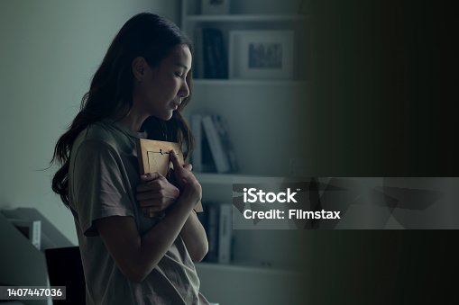 istock Asian women holding a photo frame of lost loved one and crying. 1407447036