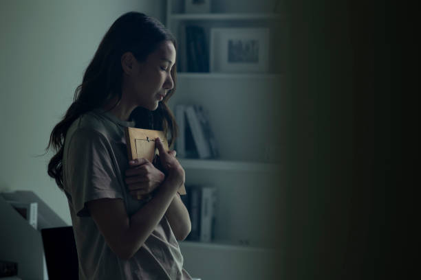 Asian women holding a photo frame of lost loved one and crying. Woman feeling sad when looking at picture of lost loved one in the frame. Depressed Asian women holding a photo frame of lost loved one and crying. squander stock pictures, royalty-free photos & images