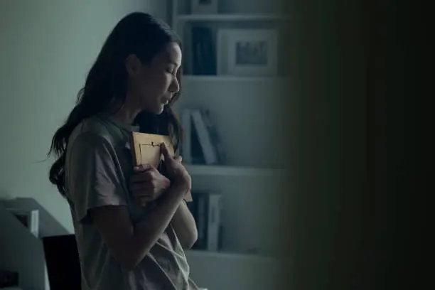 Photo of Asian women holding a photo frame of lost loved one and crying.