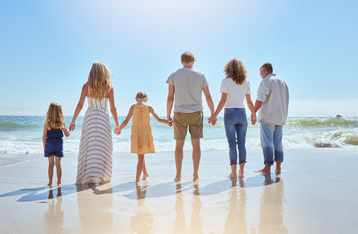 Multi generation family holding hands and walking along the beach together. Caucasian family with two children, two parents and grandparents enjoying summer vacation and standing in the ocean water