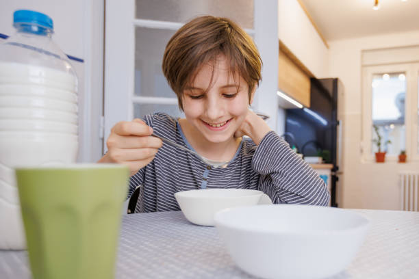 istock Happy boy sitting at the dining table at home and eating breakfast cereal by himself 1407447205