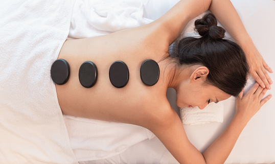 Top view of beautiful young woman lying on front with spa stones on her back, enjoying a hot stone massage. Beauty and healthcare treatment concept.
