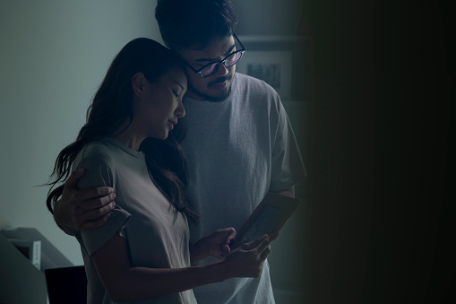 Couple feeling sad when looking at picture of lost loved one in the frame. Depressed Asian husband and wife holding a photo frame of lost loved one and crying.