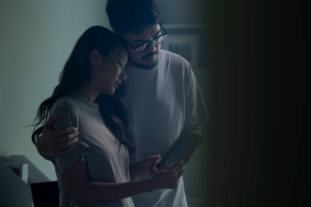 Couple feeling sad when looking at picture of lost loved one in the frame. Couple feeling sad when looking at picture of lost loved one in the frame. Depressed Asian husband and wife holding a photo frame of lost loved one and crying. worried mom with kids stock pictures, royalty-free photos & images