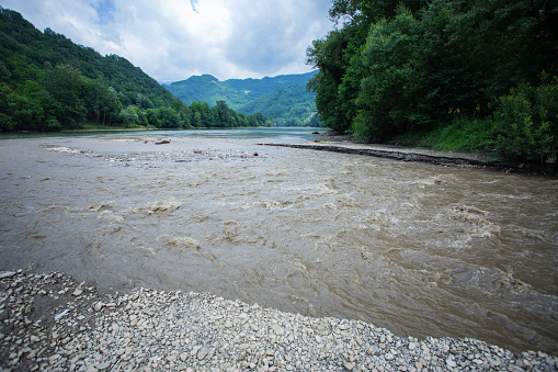 Creek in high mountains brown colored after heavy raining rushing into valley flows into big river