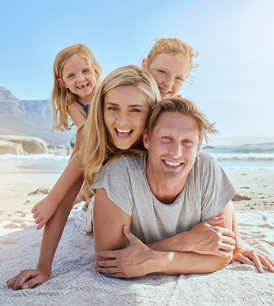 Portrait of a carefree family relaxing and bonding on the beach. Two cheerful little girls spending time with their parents on holiday. Mom and two daughters lying on top of dad enjoying vacation