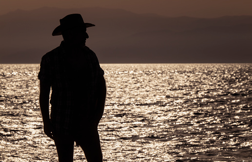 Silhouette of adult man in hat on beach during sunset