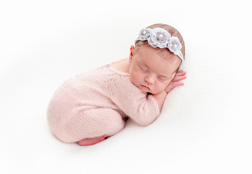 Cute newborn in pink knitted suit sleeping on stomach