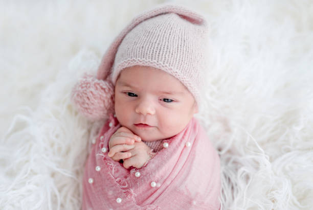 Cute awake newborn in knitted hat and decorated blanket