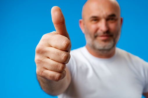 Middle age man doing happy thumbs up gesture against blue background, close up