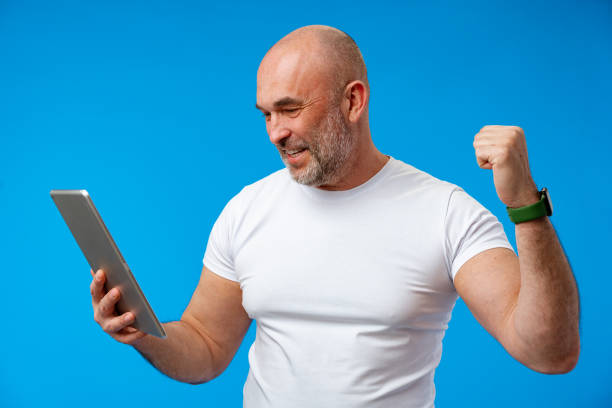 istock Handsome middle age man with digital tablet against blue background 1407454519