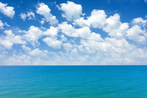 View of the sea surface and the horizon. Summer fluffy clouds over the ocean in tropical latitudes. Concept of summer vacation, travel