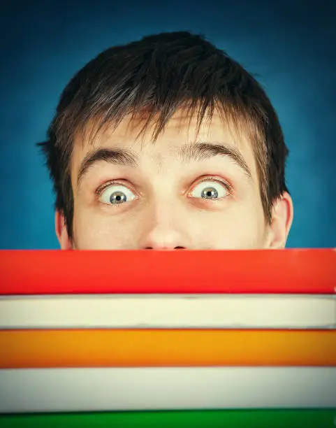 Toned Photo of Surprised Student behind the Books on the Blue Background