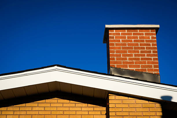 Gable of Brick House With Chimney The Gable of a brick house with brick chimney in bright sunlight, against a deep blue sky. chimney stock pictures, royalty-free photos & images