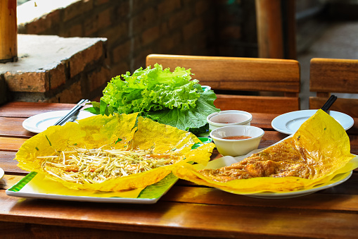Vietnamese Banh Xeo crepes filled with pork or chicken may also, shrimp, onions and bean sprouts, and hot sauce placed near the plate on the table. Food and drink concept.