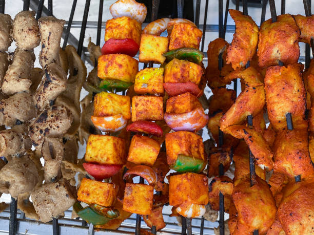 istock Full frame image of chicken and vegetable kebabs displayed on metal rack unit, chicken breast pieces chargrilled and skewered with onion and red and green peppers covered in spicy sauce at food stall, elevated view 1407467243