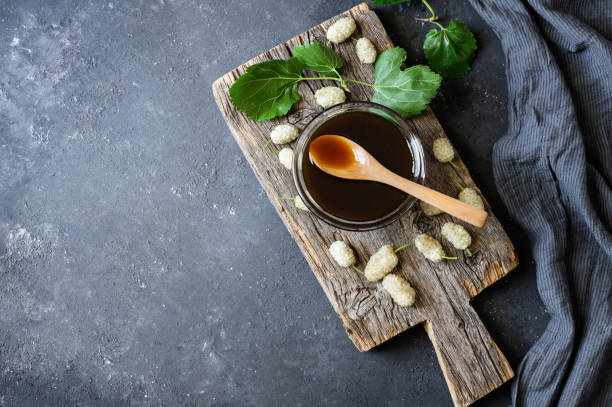 weiße maulbeermelasse in glasschüssel und holzschliff mit frischen maulbeeren, gesundes essen - molasses stock-fotos und bilder