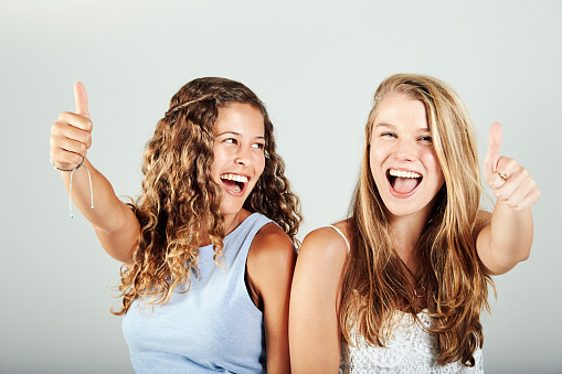 Young woman and teenage girl give a happy thumbs-up gesture.