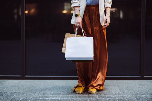 Unrecognizable businesswoman holding paper bags while standing at the city street.